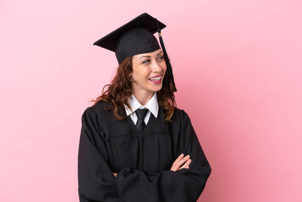 Νεαρή απόφοιτος πανεπιστημίου γυναίκα απομονωμένη σε ροζ φόντο χαρούμενη και χαμογελαστή - Φωτογραφία, εικόνα