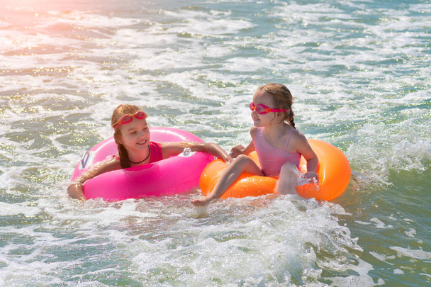İki güzel kız kardeş sahildeki deniz suyunda oynayıp eğleniyorlar. Tatil ya da tatil konsepti. Şişme yüzüklü çocuklar suda eğleniyor. - Fotoğraf, Görsel
