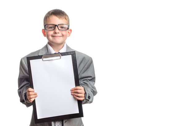 Petit garçon mignon dans des lunettes et une tablette dans ses mains habillé d'un costume gris avec une cravate sur un fond blanc. Publicité de cours éducatifs, formation avancée. - Photo, image