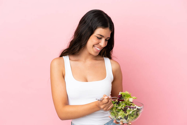 Junge kaukasische Frau isoliert auf rosa Hintergrund hält eine Schüssel Salat mit glücklichem Gesichtsausdruck - Foto, Bild