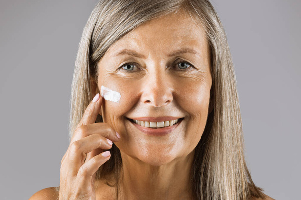 Senior lady smiling and looking at camera with cream on face - Zdjęcie, obraz