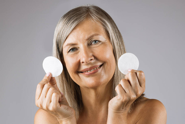 Aged woman posing in studio with cotton pads in hands - Photo, image