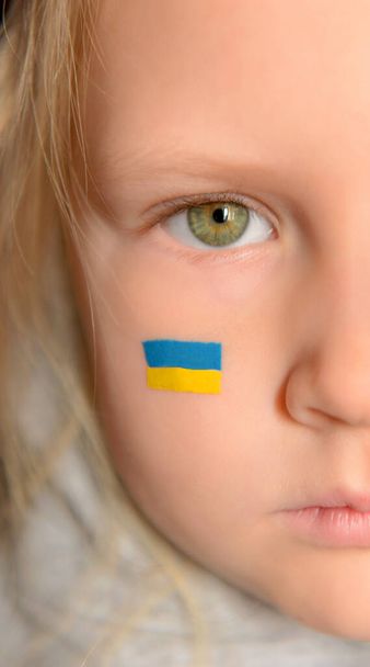 Metade do rosto de uma menina ucraniana com uma bandeira pintada na bochecha. Rezai pela Ucrânia.  - Foto, Imagem