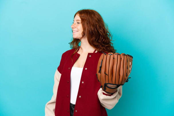 Adolescente rousse fille avec gant de baseball isolé sur fond bleu regardant côté - Photo, image