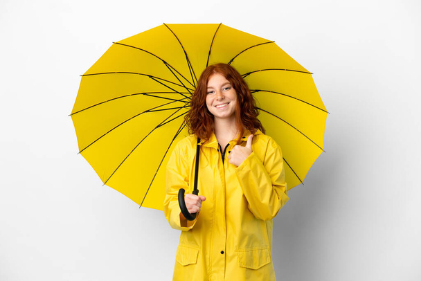 Adolescente ruiva menina capa impermeável e guarda-chuva isolado no fundo branco dando um gesto polegares para cima - Foto, Imagem
