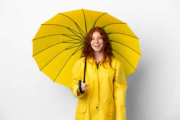 Подростковая рыжая девушка дождливое пальто и зонтик изолированы на белом фоне с удивительным выражением лица - Фото, изображение