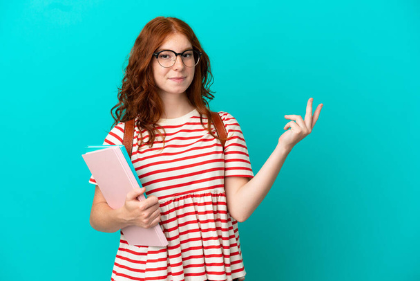 Opiskelija teini punapää tyttö eristetty sinisellä taustalla ulottuu kädet sivulle kutsuvan tulla - Valokuva, kuva