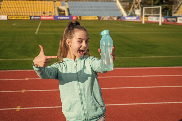 Happy girl child in activewear stand at sports stadium pointing finger at sport water bottle, hydration - Foto, Imagem