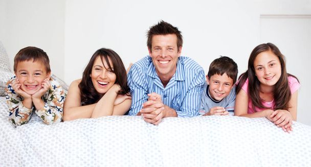 Ci aggiorniamo alla fine della giornata. Una famiglia amorevole di cinque persone sdraiate a letto insieme indossando un pigiama. - Foto, immagini