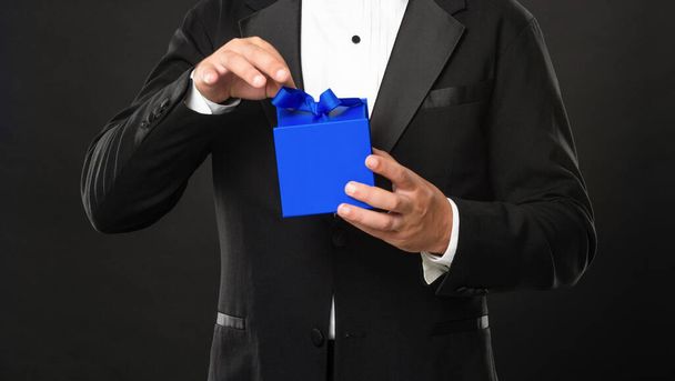 cropped man in tuxedo bow tie on black background open business reward box. occasion greeting. - Foto, immagini