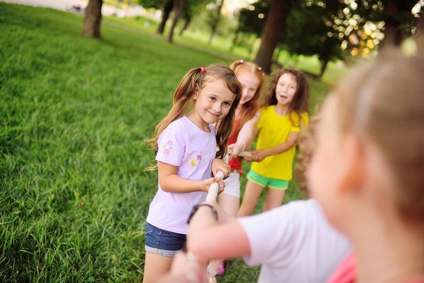 a group of children compete in a tug of war in the open air against the background of grass and park. - Zdjęcie, obraz