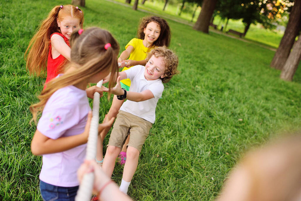 group of preschool children - boys and girls compete in a tug of war against the background of a park and greenery. - Foto, Imagen