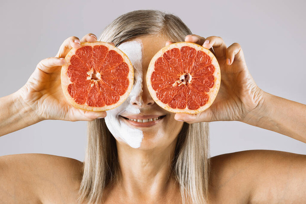 Aged woman with face mask covering eyes with grapefruit - 写真・画像