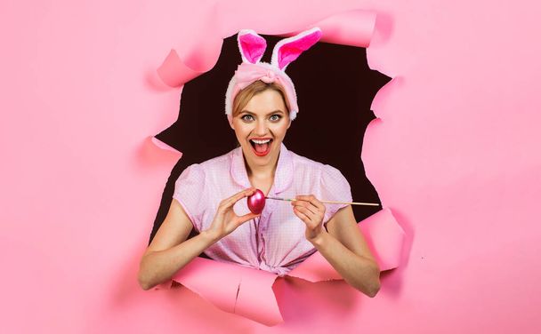 ハッピー・イースター。ウサギの耳に卵を描く笑顔の女の子。ピンクの卵と絵筆を持つウサギの女性. - 写真・画像
