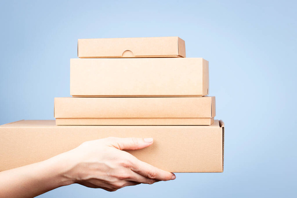 Montón de cajas de cartón en manos femeninas. Cajas de paquete marrón en blanco sobre fondo azul claro. Paquete, compras, envío gratis, concepto de entrega - Foto, Imagen