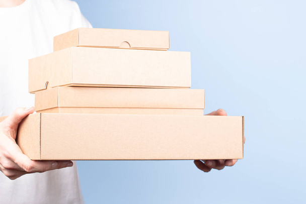 Stapeln von Kartons in weiblichen Händen. Leere braune Paketkästen auf hellblauem Hintergrund. Verpackung, Einkauf, kostenloser Versand, Lieferkonzept - Foto, Bild