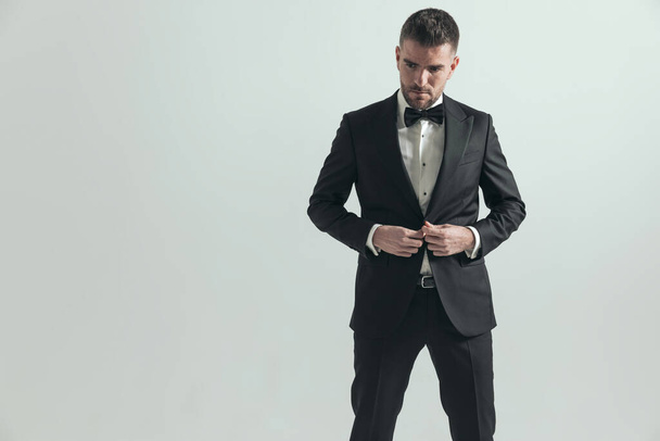 dramatic businessman fixing his jacket while looking down and wearing a black tuxedo - Photo, Image