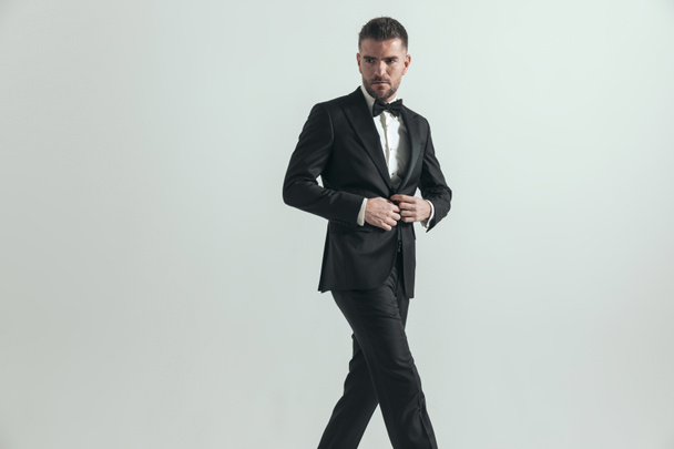 sexy handsome businessman looking away, opening his jacket and crossing his legs against gray background - Photo, image