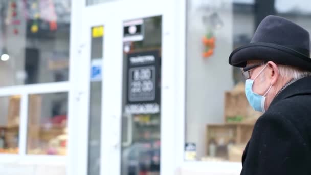 Een gepensioneerde loopt in quarantaine door de straten van een Europese stad. Opa met een beschermend masker - Video