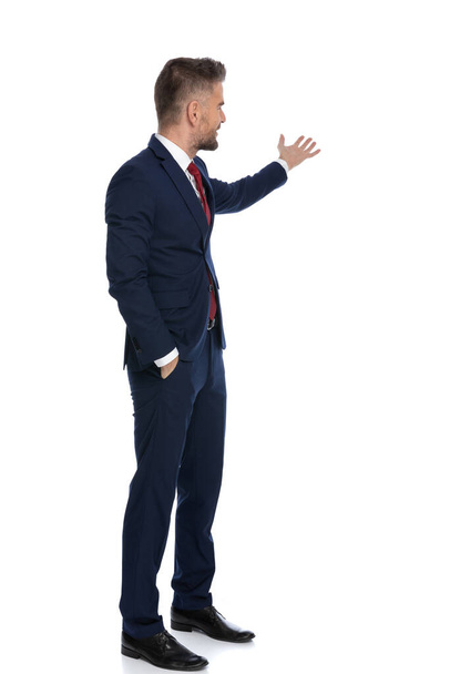 attractive businessman presenting us something to the side and holding one hand in the pocket - Фото, изображение