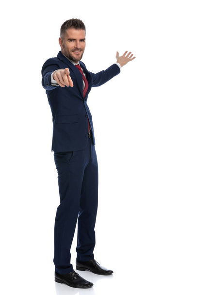 young businessman gesturing you, come with me and smiling against white studio background - Foto, Imagen