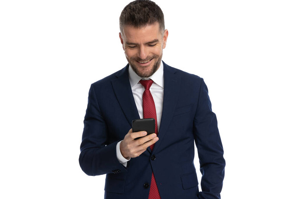 aantrekkelijke zakenman kijken naar de telefoon en het gevoel blij van wat hij ziet op witte achtergrond - Foto, afbeelding