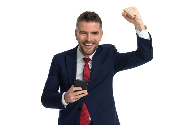 attraente uomo d'affari celebrando il successo e tenendo un telefono su sfondo bianco - Foto, immagini