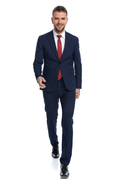 joven hombre de negocios guapo caminando hacia la cámara con una gran sonrisa en su cara contra el fondo blanco - Foto, imagen