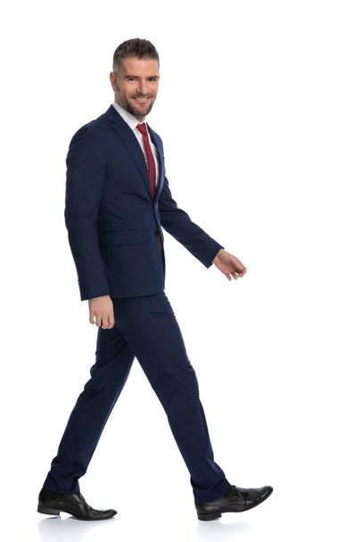 homme d'affaires heureux marchant sur le côté avec un sourire sur son visage sur fond blanc - Photo, image