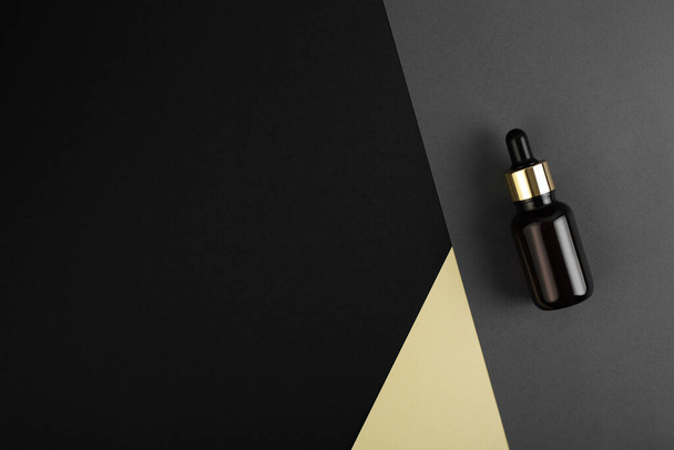 glass brown bottle with pipette with essential oil on a grey, black geometric background top view. Aromatic cosmetic product for skin and hair care Moisturizing beauty product with organic natural oil. - Photo, Image