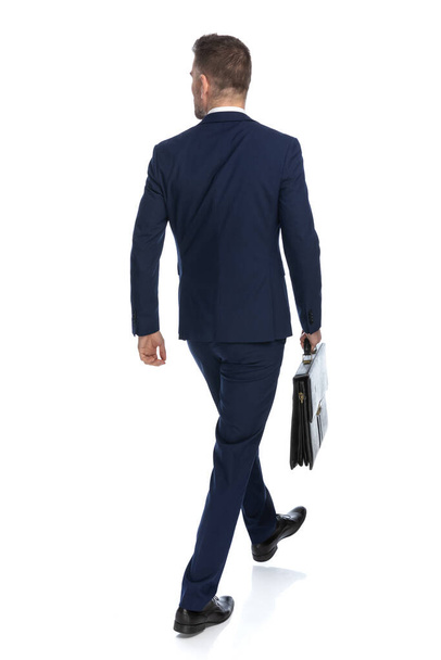 rear view of a businessman walking one way and looking the other with a case in hand  - Photo, Image