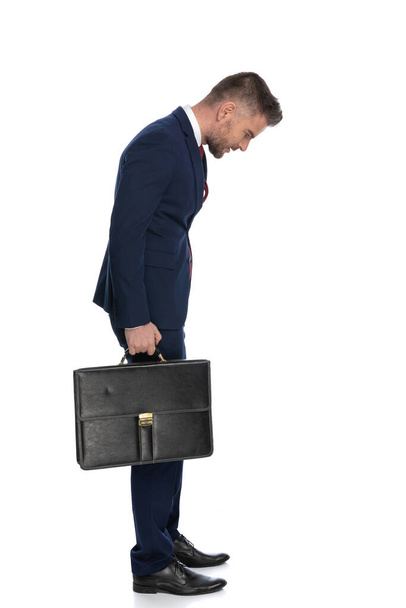 side view of a businessman stopping for a second and checking out what's down while holding a case - Foto, Imagem