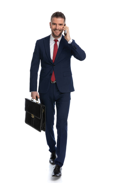 happy businessman going to close the deal with his case with him and talking on the phone - Foto, Imagem