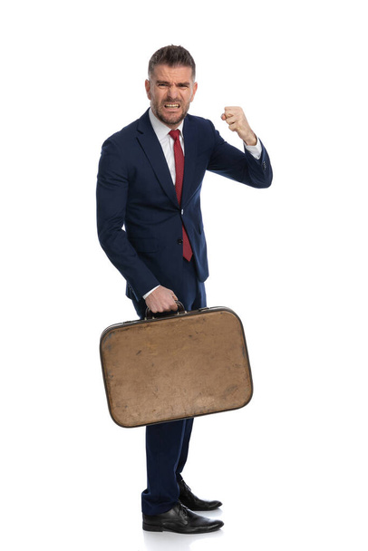 businessman threatening with his fist raised and being very aggressive and upset, holding a luggage - Foto, afbeelding