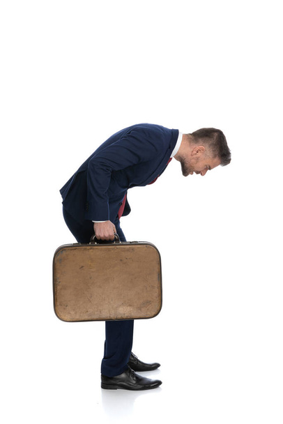 vista lateral de un hombre de negocios mirando hacia abajo a algo y sintiéndose perplejo mientras sostiene su equipaje - Foto, imagen
