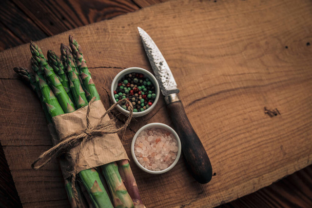 vista superior de los cuencos de sal y pimienta entre verduras frescas y un cuchillo en la parte superior de una tabla de cortar rústico - Foto, Imagen