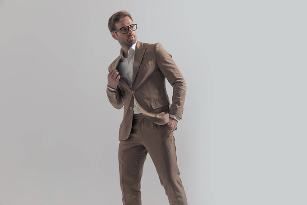 Seitenansicht eines attraktiven Geschäftsmannes, der zurückblickt, über die Schulter schaut und seinen Anzug in einer Mode-Pose fixiert - Foto, Bild