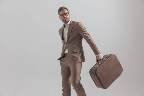 セクシーなファッションモデルポーズで彼のスーツケースでスポットライトと手でポケットに灰色の背景 - 写真・画像
