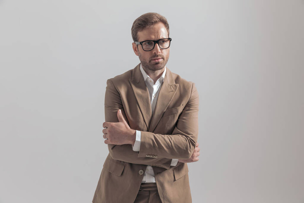 attraktiver Geschäftsmann verschränkt die Arme vor der Brust, schaut weg und trägt eine Brille auf grauem Hintergrund - Foto, Bild