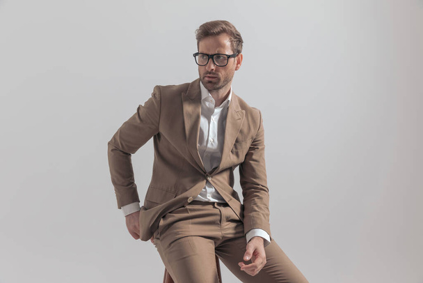handsome businessman with tough attitude having a firm posture on the chair, looking away and wearing eyeglasses - Photo, Image