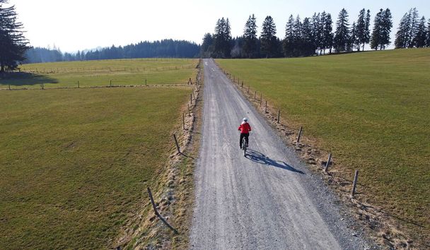 Yalnız yoldaki gölgeli kadın bisikletçinin hava aracı görüntüsü.  - Fotoğraf, Görsel