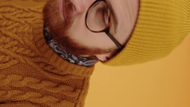 Young attractive European man looks at the camera, takes off his glasses and winks yellow background studio shot vertical video  - Footage, Video