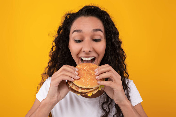 Funny latina dama celebración hamburguesa mordiendo sándwich en el estudio - Foto, imagen