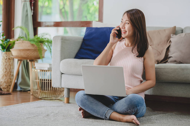 Piękna Azjatka rozmawia na smartfonie pracując z notebookiem w domu - Zdjęcie, obraz