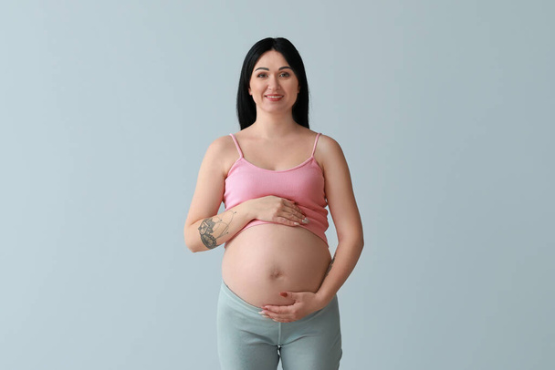 Έγκυος νεαρή γυναίκα σε γκρι φόντο - Φωτογραφία, εικόνα