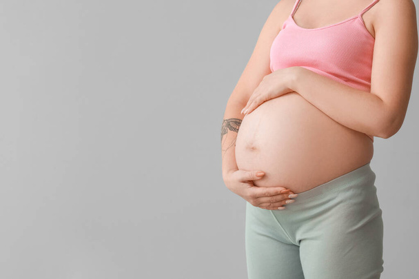 Mujer joven embarazada sobre fondo gris - Foto, imagen