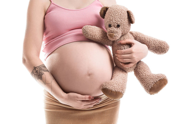 Mujer joven embarazada con oso de peluche aislado en blanco - Foto, Imagen
