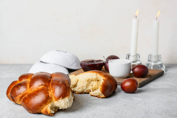 Παραδοσιακό ψωμί χαλάχ με λαμπυρίζοντα κεριά και εβραϊκά καπάκια σε ελαφρύ φόντο. Σαμπάτ Σαλόμ. - Φωτογραφία, εικόνα