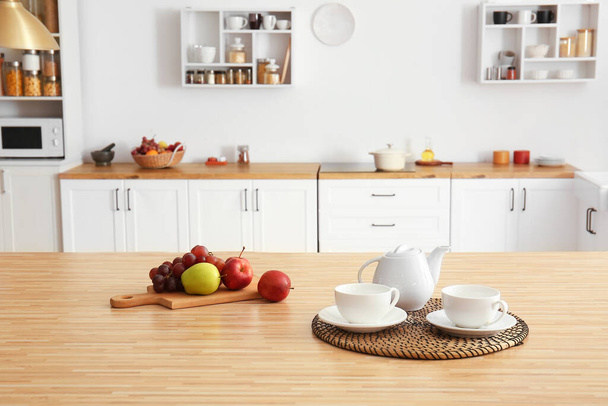 Teáskanna csészékkel, étellel és gyümölcsökkel az étkezőasztalon a konyhában - Fotó, kép