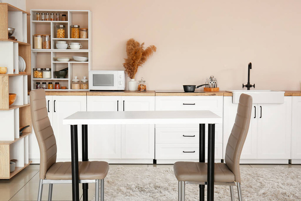 Intérieur de cuisine élégante avec comptoirs blancs, étagères et table à manger - Photo, image